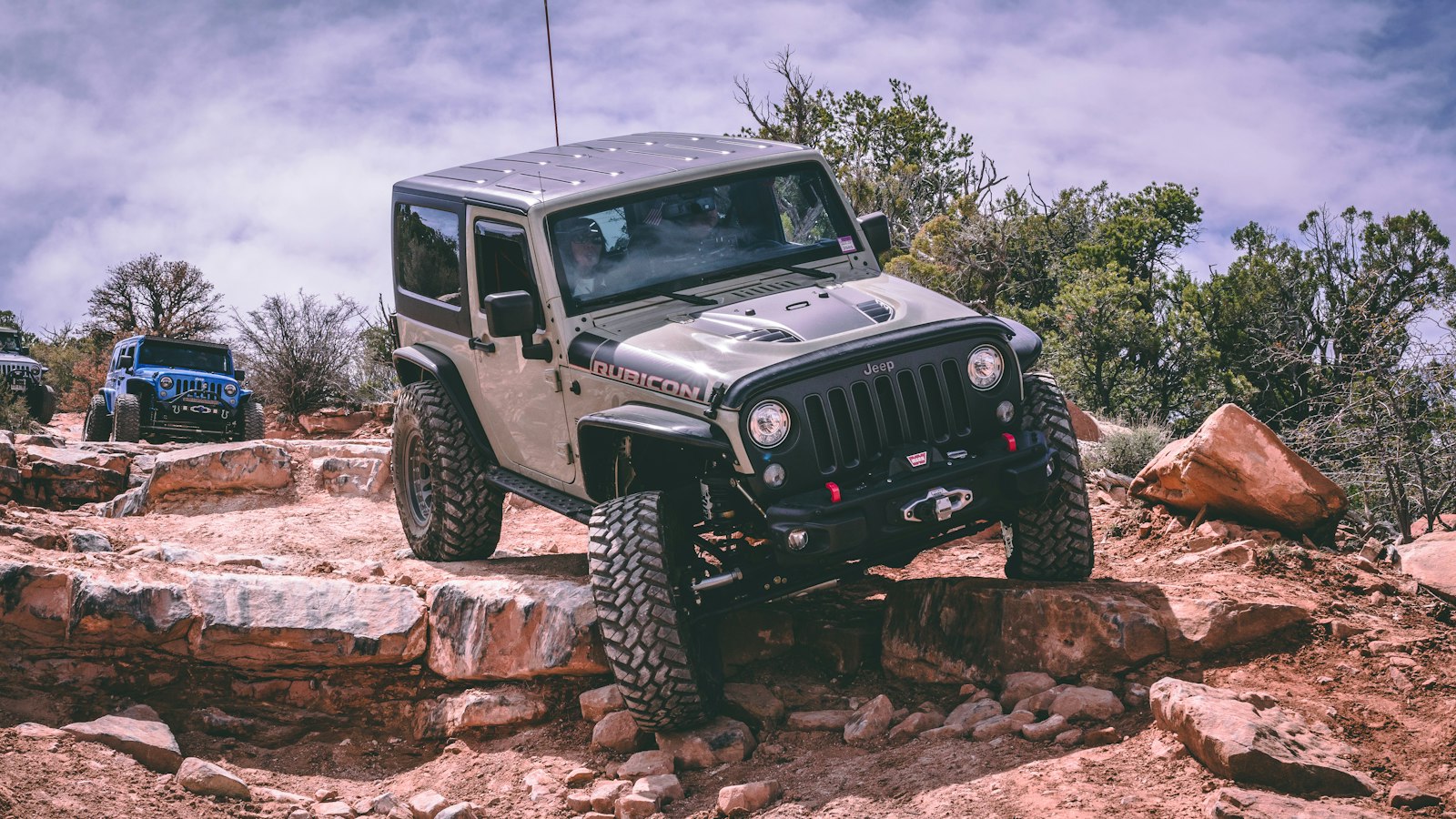 Jeep Wrangler climbing a rocky ledge on a trail