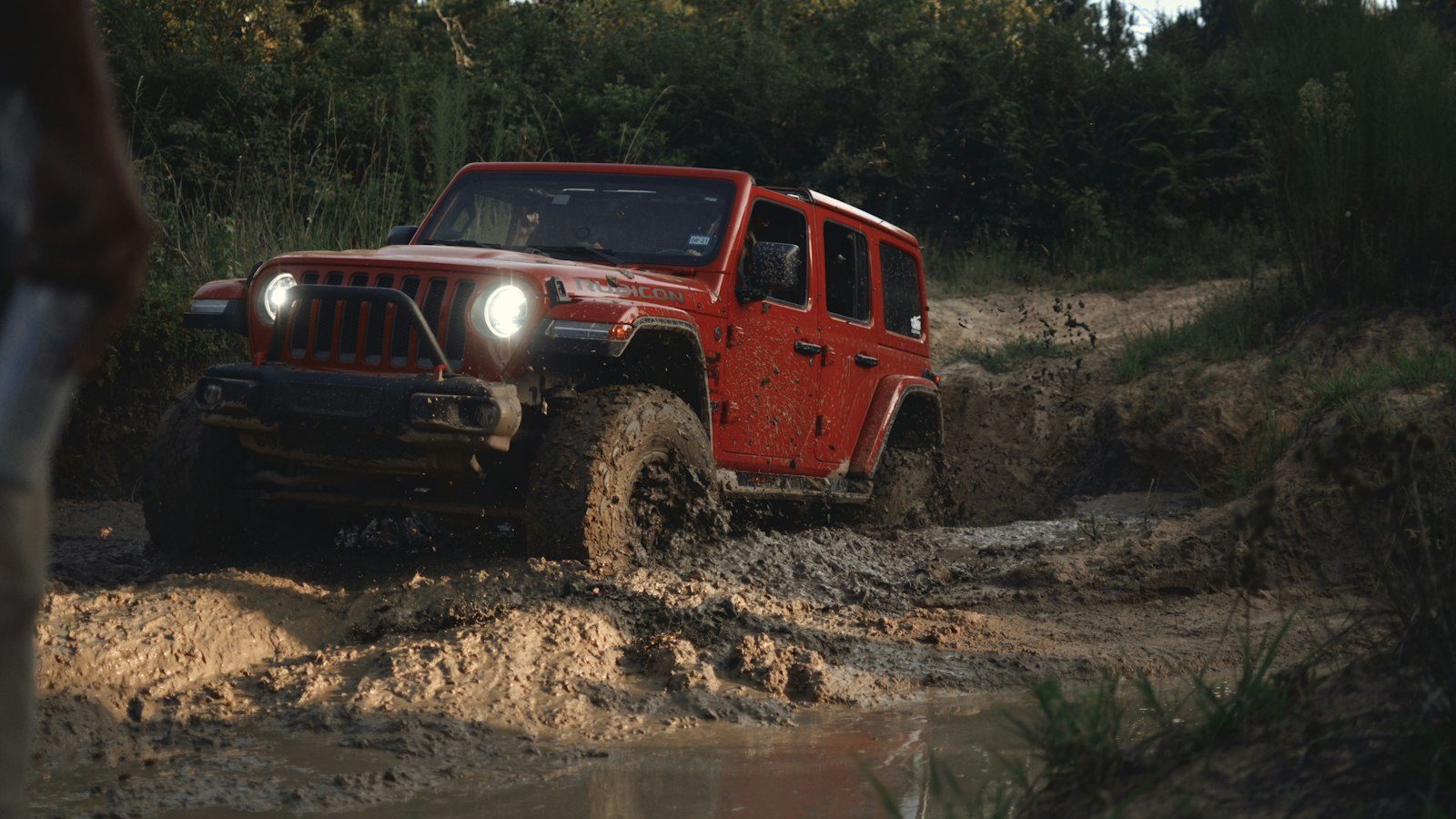 Red Jeep Wrangler working through a muddy, rutted trail