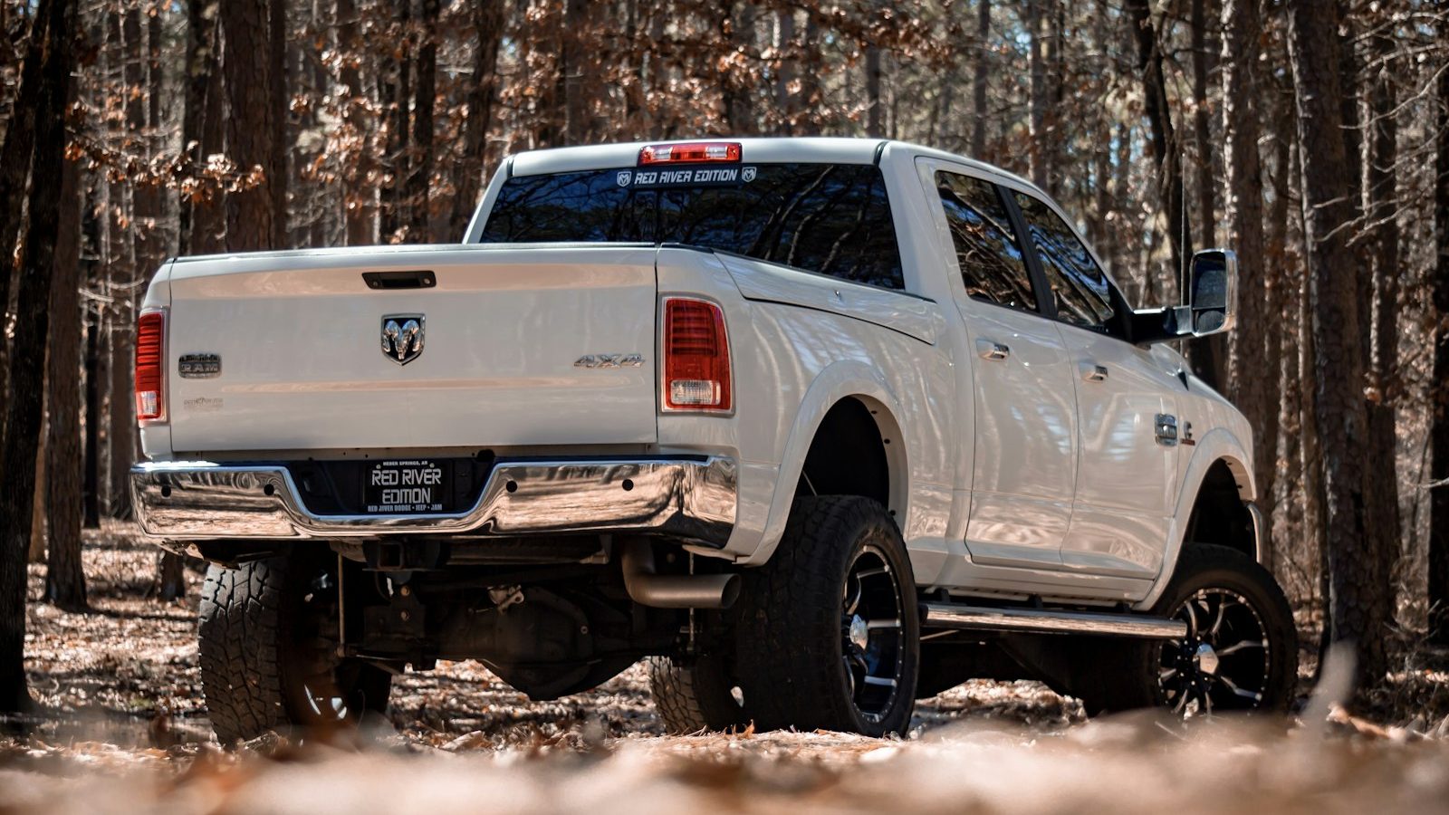 Lifted white Ram pickup on large off-road tires in a forest