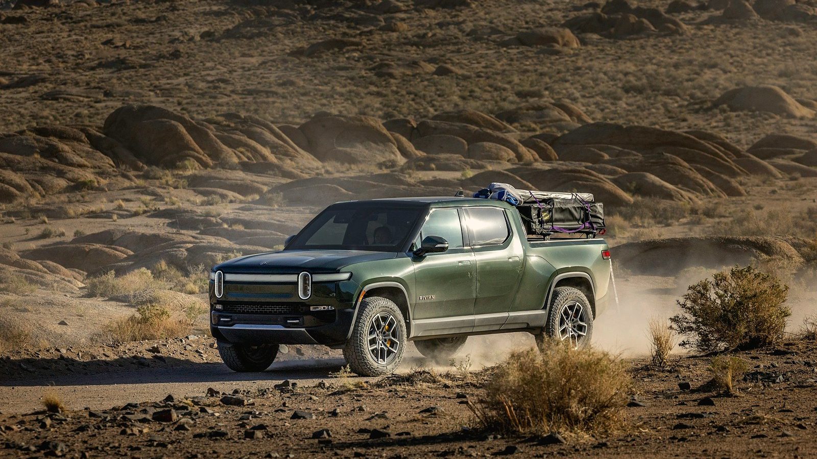 Green Rivian R1T electric pickup kicking up dust on a desert dirt trail